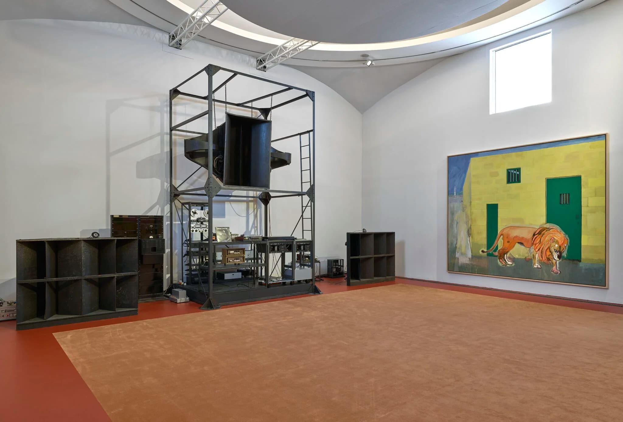 A room at “House of Music”: a funnel-shaped 1920s cinema speaker suspended from a steel frame over racks of vintage sound equipment; in the background, two empty wooden shelving units and a Peter Doig painting on the wall