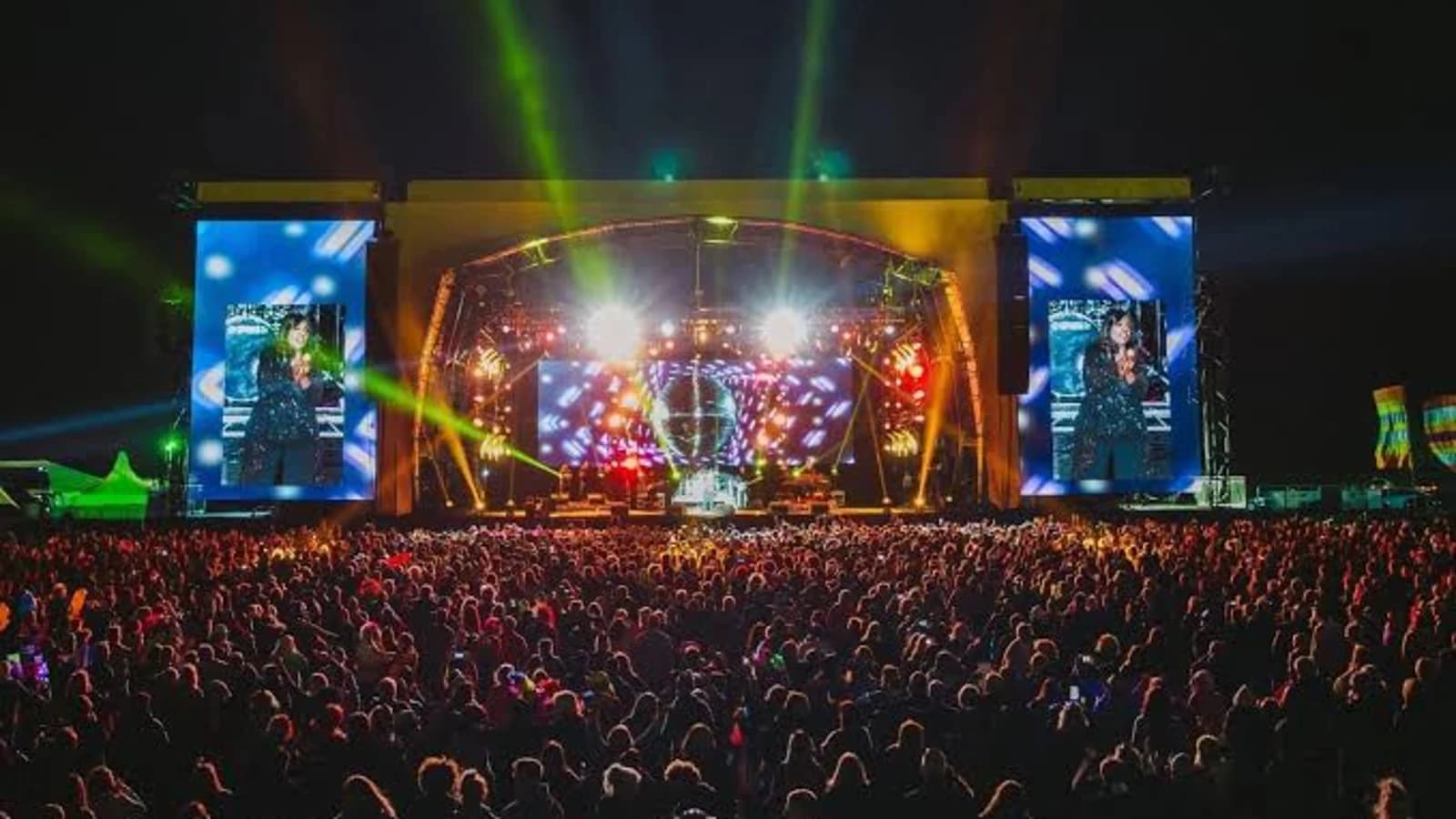 Escenario principal del Rewind Festival de noche, con haces de luz verdes y amarillos sobre la multitud y pantallas laterales gigantes