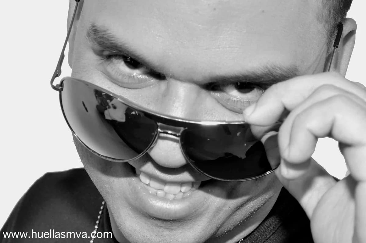 DJ DrumsMaster en retrato blanco y negro, sonriendo mientras se baja los lentes de aviador