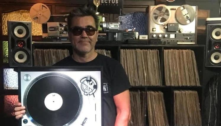 Pedro Neira, creador de Macro Efectus, en su estudio: sostiene un cuadro con un plato tornamesa frente a una pared de vinilos, grabadoras de carrete abierto y el logotipo «EFECTUS»
