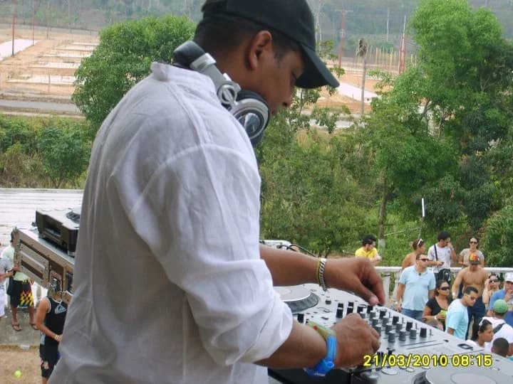 Robert Yance de camisa blanca, mezclando de día en una cabina al aire libre con público detrás