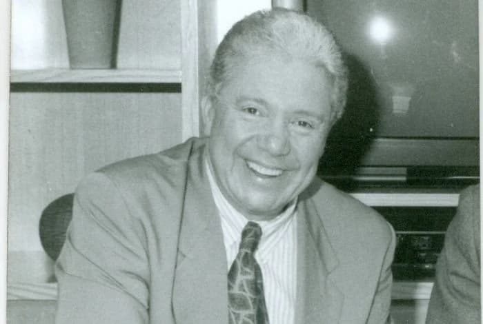 Retrato en blanco y negro de Guillermo «Fantástico» González sonriendo, con traje y corbata, en los estudios de televisión
