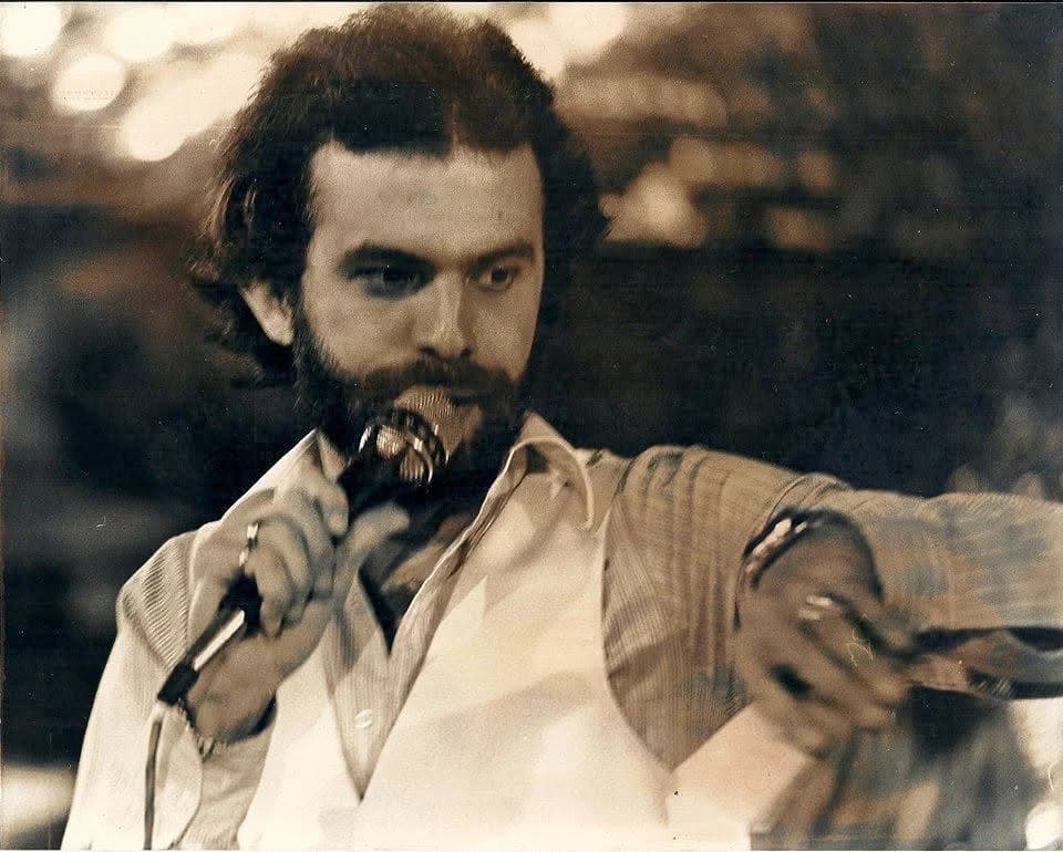 Gustavo Pierral in full flow as host, microphone in hand and his arm stretched out toward the audience — the announcer of “Disco Fiebre,” period photograph in sepia