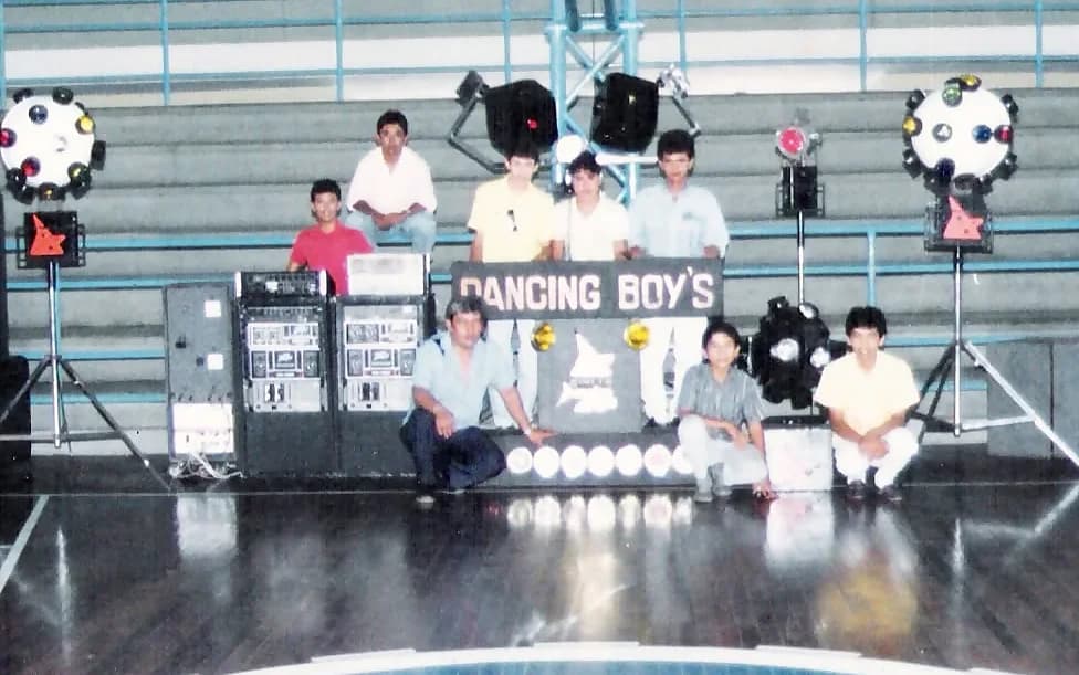 Miniteca Dancing Boy's — ocho integrantes posando junto al mueble y las torres de sonido, en las gradas de un gimnasio cubierto, fotografía de archivo