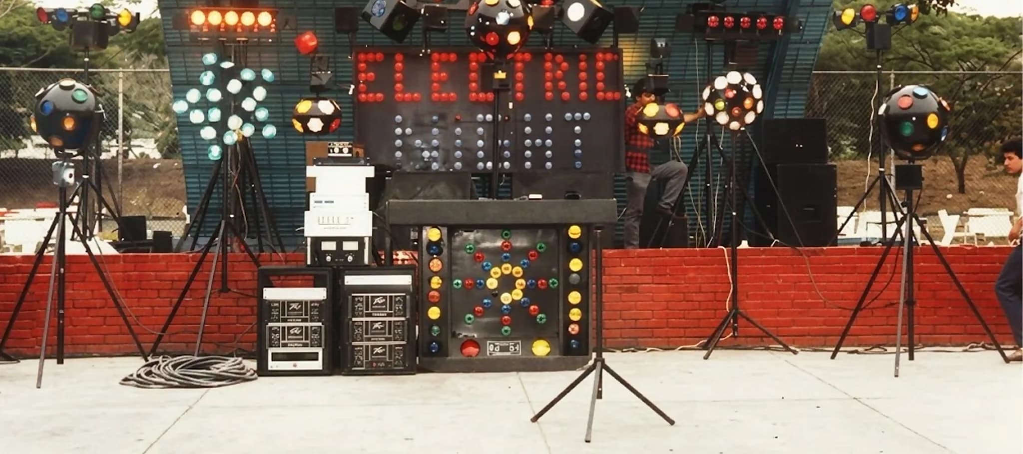 Miniteca Electric Night — el letrero de bombillos «Electric Night» sobre la cabina, flanqueado por luces robóticas y esferas de espejos, fotografía de archivo