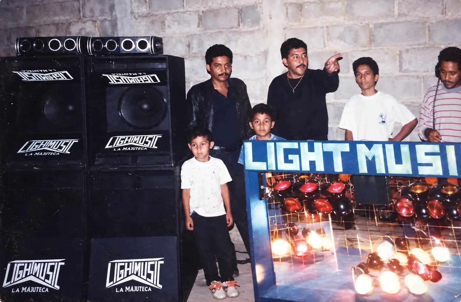 Miniteca Light Music — members and friends posing beside the speakers lettered “Lightmusic, La Majuteca” and the illuminated “Light Musi[c]” sign, archive photograph