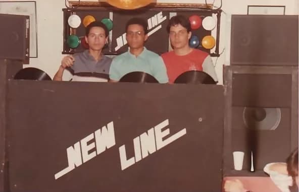 Miniteca New Line — la cabina rotulada «NEW LINE» con tres integrantes detrás sosteniendo discos de vinilo, entre los bafles y el panel de luces de colores