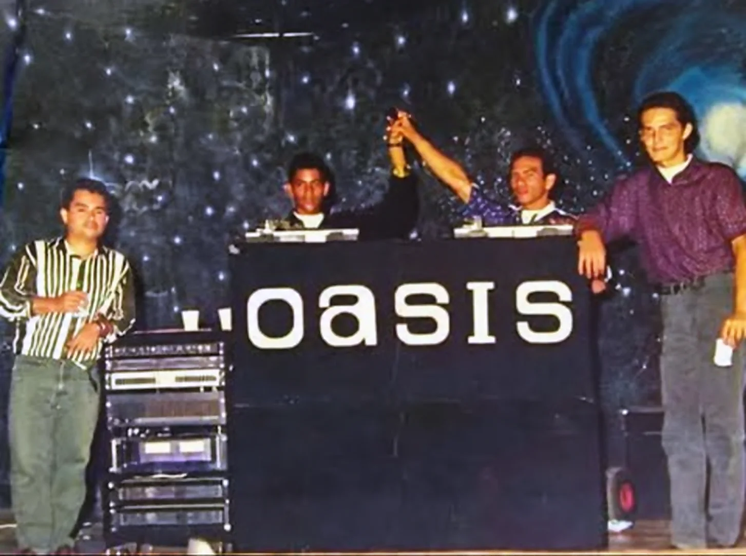 Miniteca Oasis — cuatro integrantes tras el mueble «Oasis», uno de ellos alzando un trofeo, con telón de fondo estrellado, fotografía de archivo