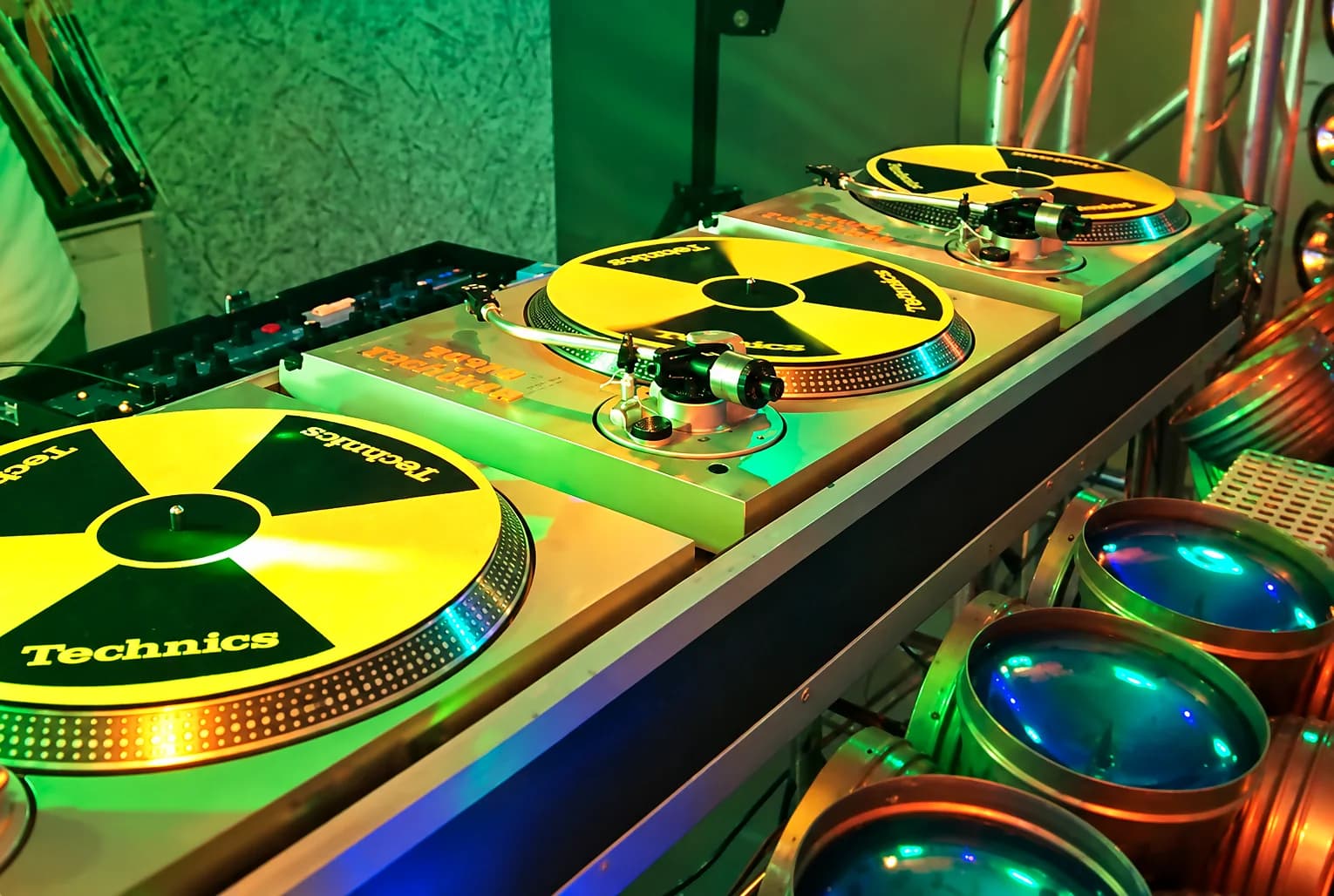 Miniteca Rigel — tres tornamesas Technics con slipmats amarillos y negros, bajo luces verdes y azules, fotografía de archivo