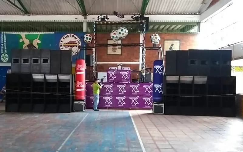 El sistema de la Miniteca Stereos 1090 montado en el patio techado del Colegio INEM de Cúcuta: dos torres de bafles apilados flanqueando la cabina, con la estructura de luces y bolas de espejo en lo alto