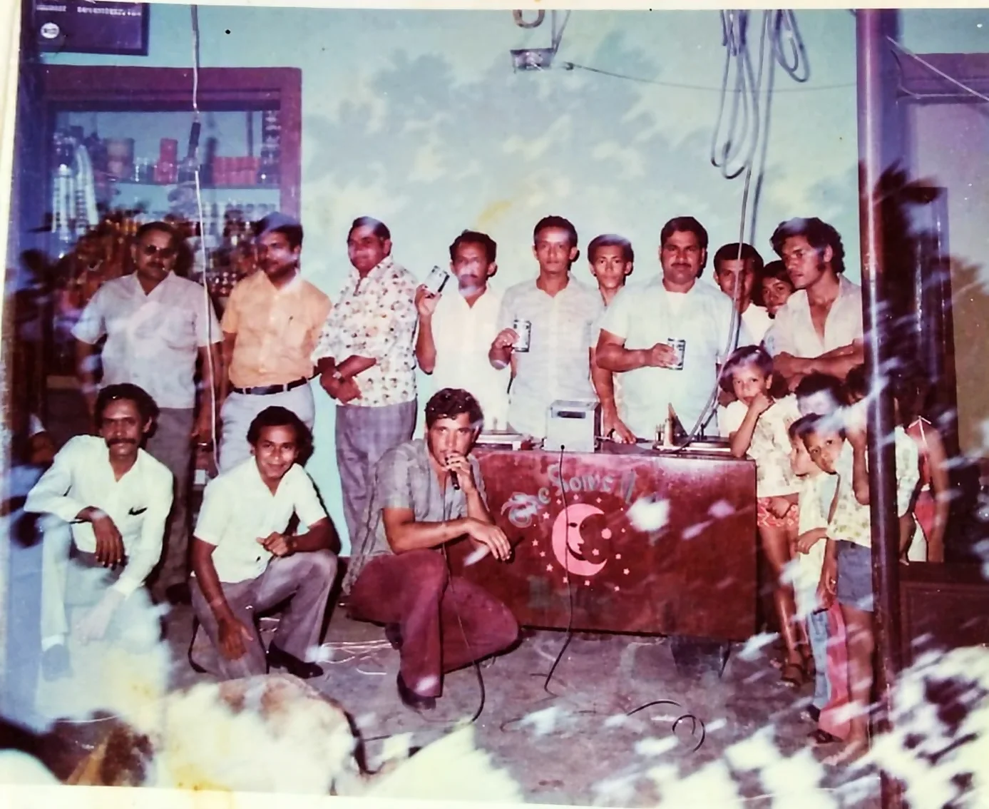 Miniteca The Son's Night — grupo numeroso posando junto al mueble con el símbolo de luna creciente, entre ellos un animador con micrófono en primer plano, fotografía de archivo de 1974