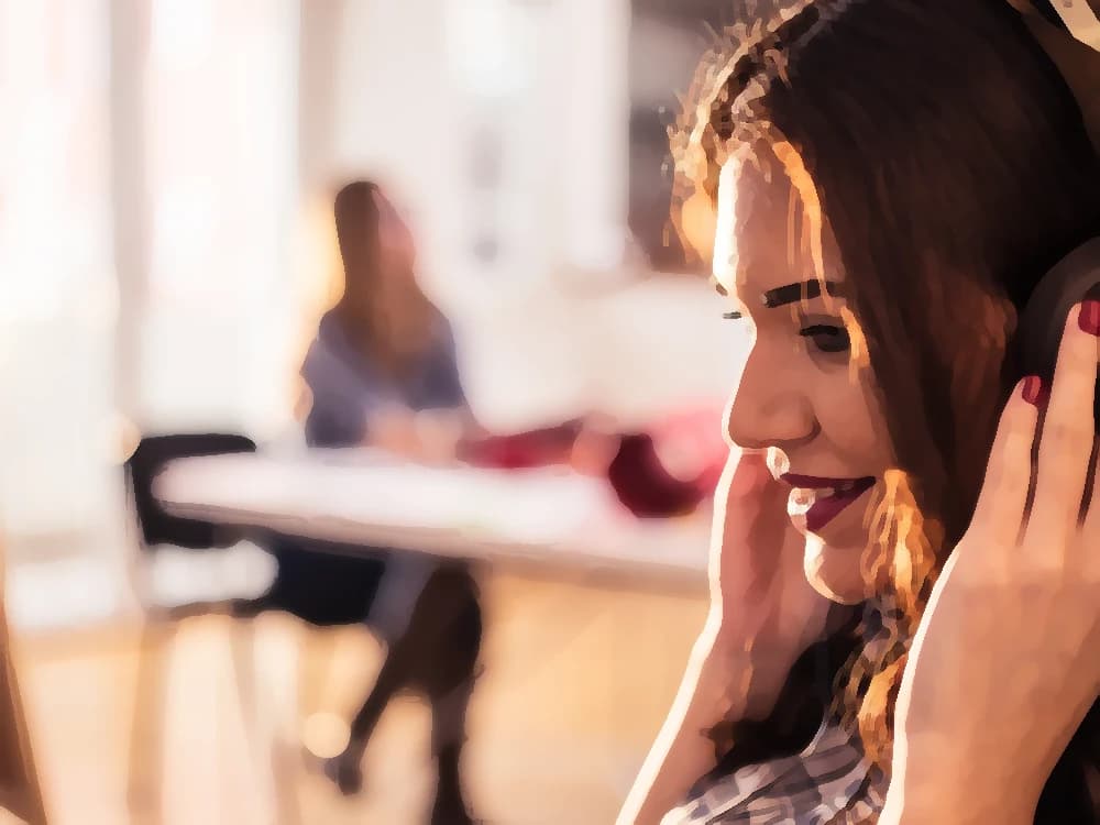 A young woman smiles with her headphones on in an office bathed in afternoon sun, a colleague out of focus in the background — cover art of the CMTK Radio show Clásicos de Oficina — Sin Repetición