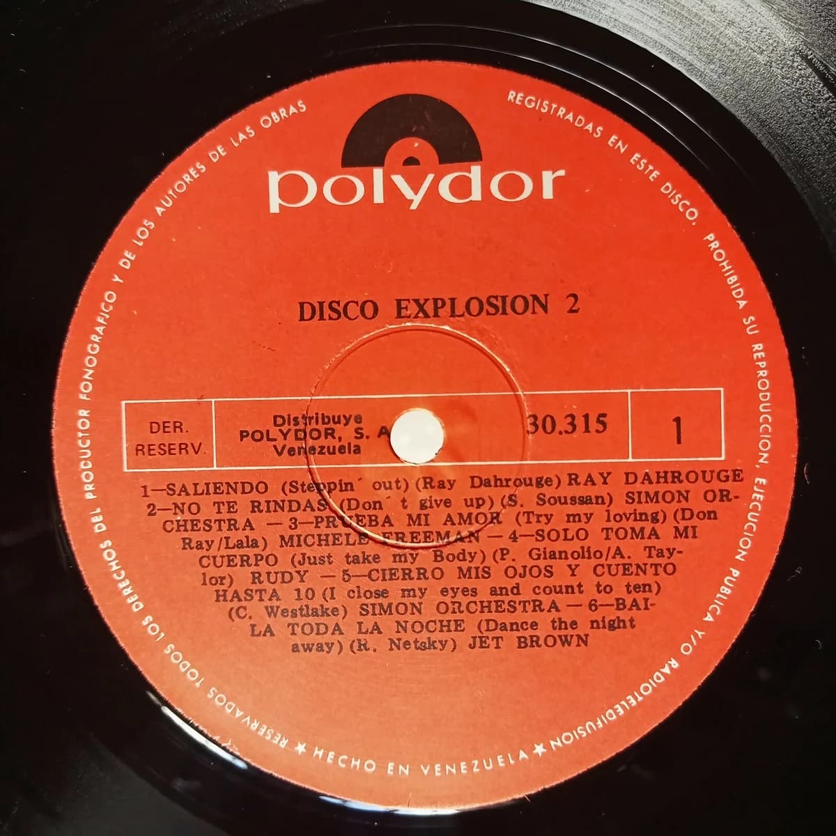 Disco Explosion Vol. 2 — Archivo CMTK Etiqueta naranja de Polydor del Lado 1 de «Disco Explosion 2», con los seis temas listados en español y su título original en inglés entre paréntesis