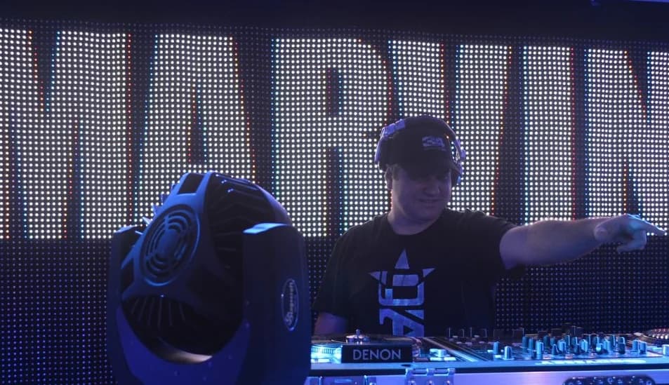 Marvin Presutti en cabina con gorra y camiseta negra, junto a un cabezal de luces, ante una pantalla LED gigante que deletrea «MARVIN» Marvin Presutti en cabina con gorra y camiseta negra, junto a un cabezal de luces, ante una pantalla LED gigante que deletrea «MARVIN»