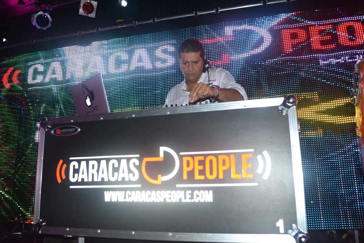 Mike Raymond en cabina tras su computadora, con un flight case rotulado «Caracas People» al frente, ante una pared de video LED Mike Raymond en cabina tras su computadora, con un flight case rotulado «Caracas People» al frente, ante una pared de video LED