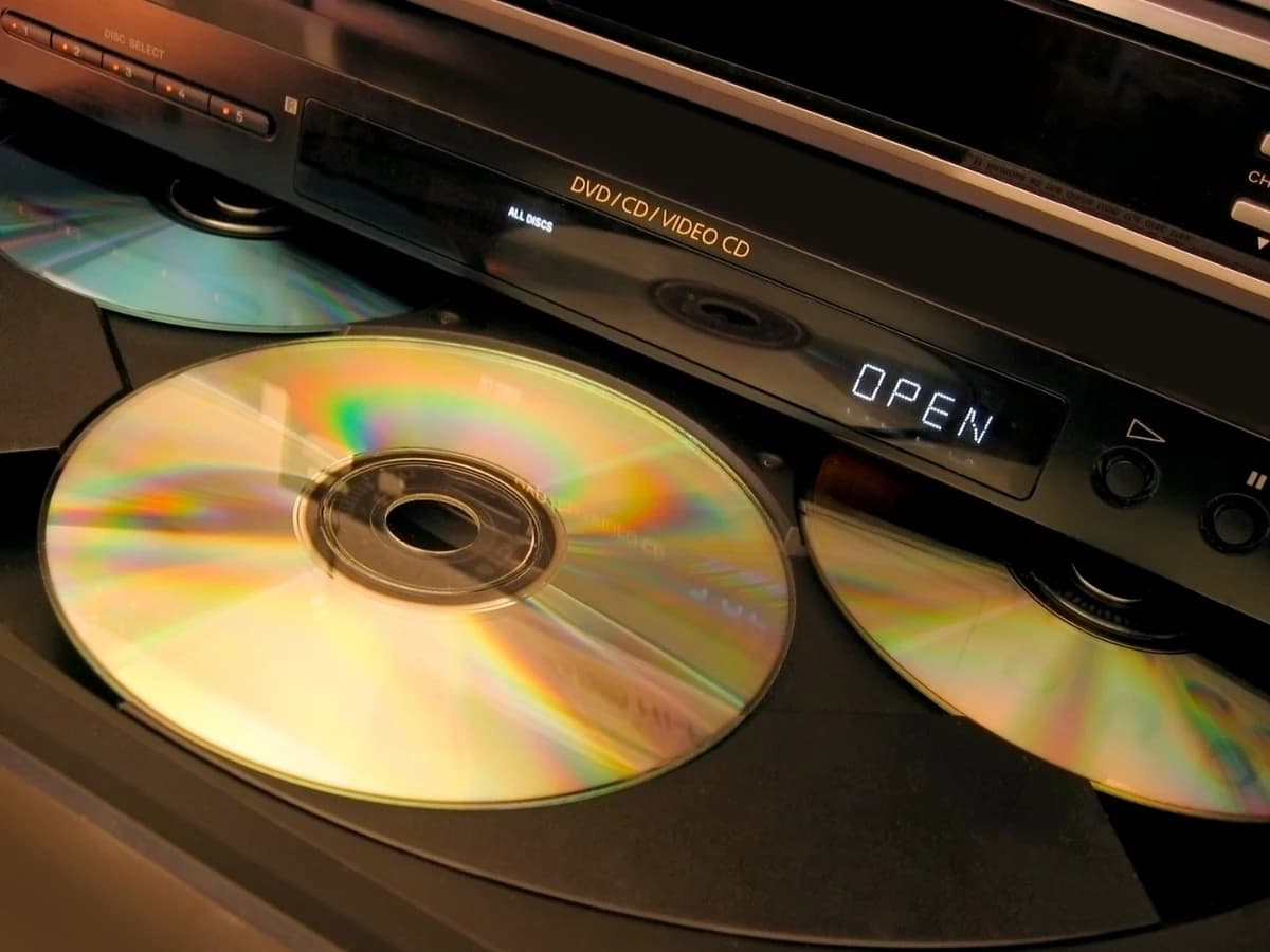 La bandeja abierta de un reproductor de discos compactos con tres CD en el carrusel, el frontal rotulado «DVD / CD / VIDEO CD» y el display encendido en «OPEN» La bandeja abierta de un reproductor de discos compactos con tres CD en el carrusel, el frontal rotulado «DVD / CD / VIDEO CD» y el display encendido en «OPEN»