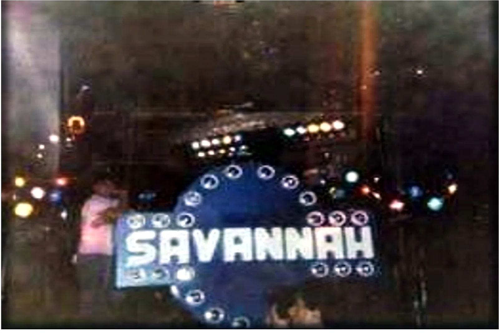 Miniteca Savannah — la consola con el nombre en letras luminosas y aros de luces, fotografiada de noche en plena presentación Miniteca Savannah — la consola con el nombre en letras luminosas y aros de luces, fotografiada de noche en plena presentación